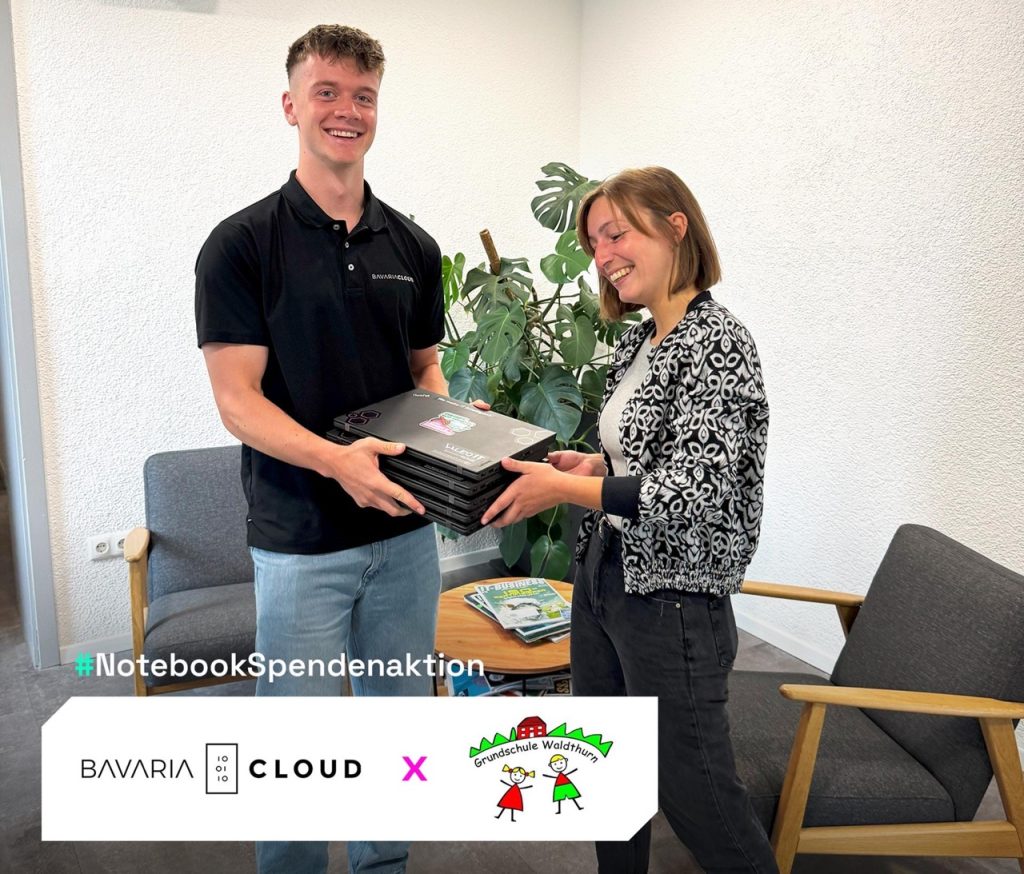 BavariaCloud-Azubi übergibt gespendete Notebooks an eine Vertreterin der Grundschule Waldthurn im Rahmen der NotebookSpendenaktion