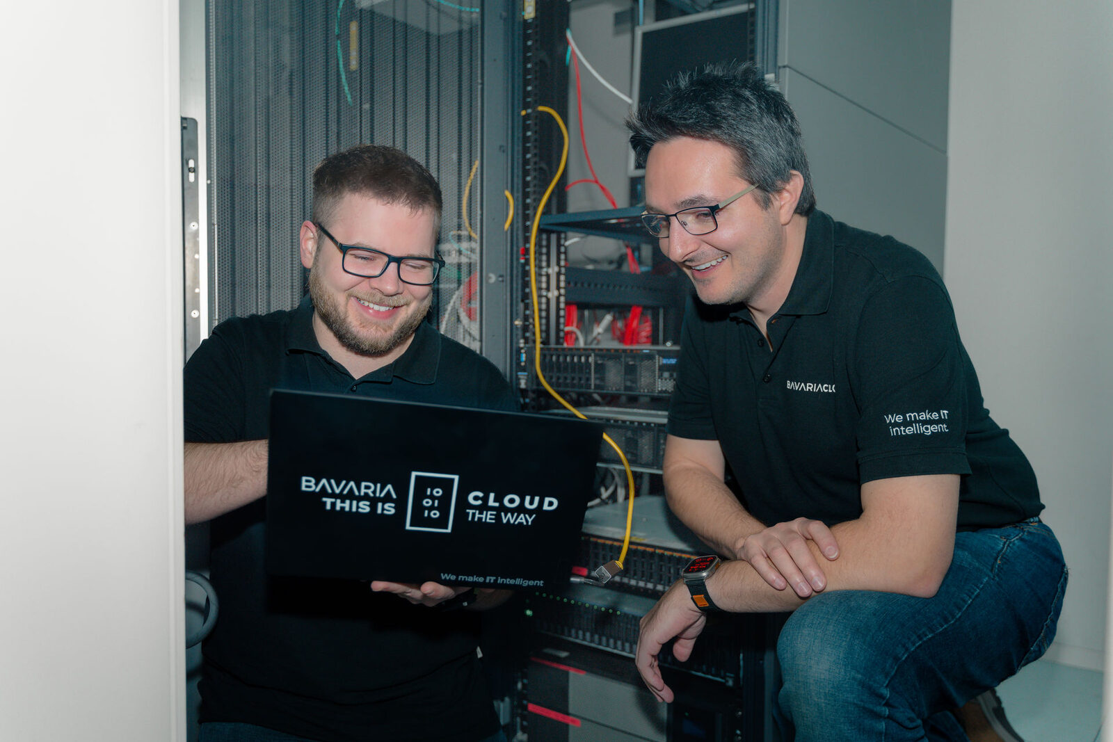 Zwei BavariaCloud-Mitarbeiter prüfen gemeinsam eine E-Mail am Laptop vor einem Serverschrank