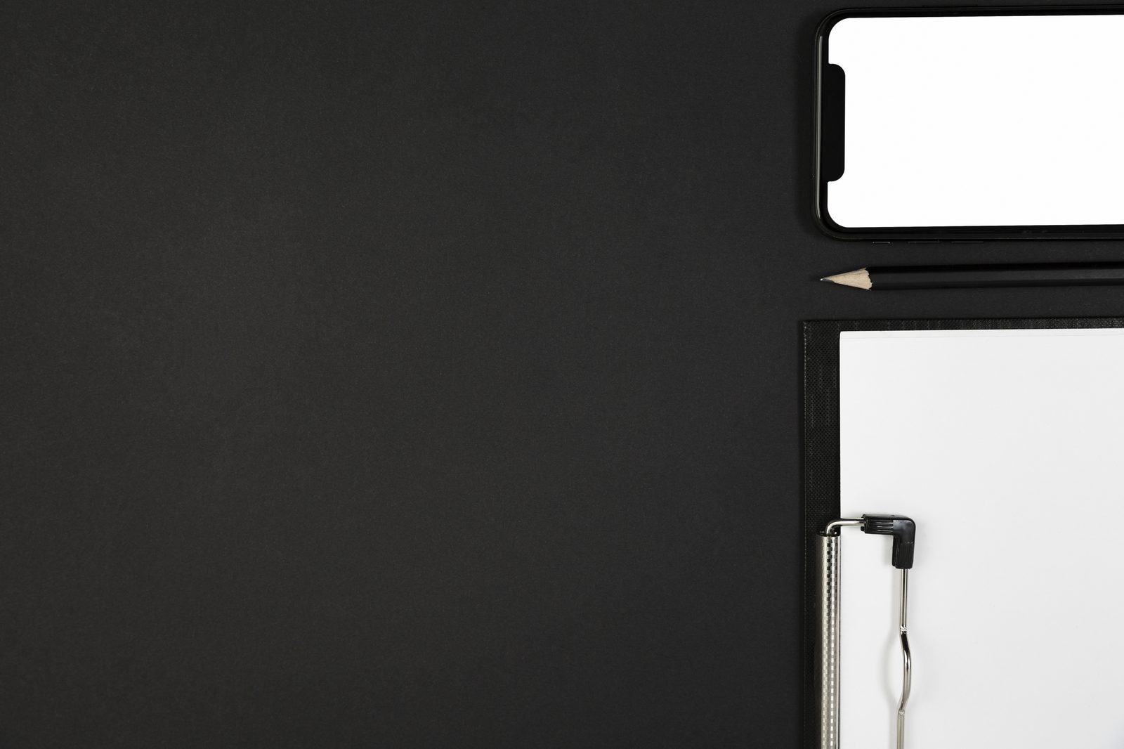 Dunkler Schreibtisch mit Notizblock, Stift und Smartphone von oben